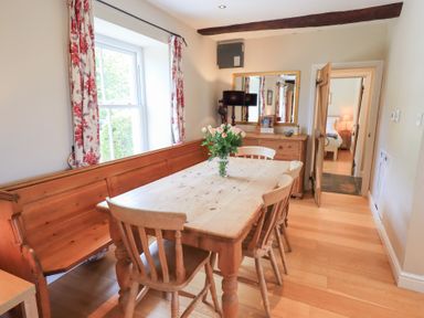 A dining room with a wooden table surrounded by chairs and a bench with a vase of flowers on the table at Mell View Cottage Ullswater