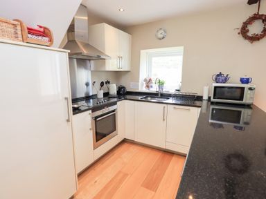 A kitchen with white cabinets black countertops oven microwave kettle and window at Mell View Cottage in Ullswater