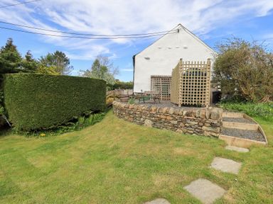 A green hedge and stone wall surrounding a gravel seating area next to a white building at Mell View Cottage in Ullswater
