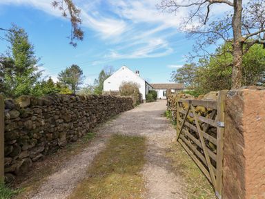 A gravel driveway bordered by stone walls leading to a white house with a wooden gate at Mell View Cottage in Ullswater
