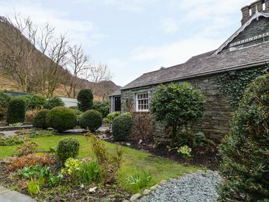 A garden with bushes and trees beside a stone building at Coombe Cottage in Borrowdale