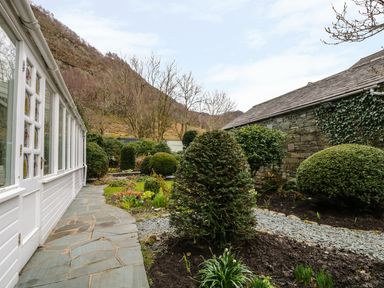 A garden with stone path shrubs and a white building with glass windows at Coombe Cottage in Borrowdale