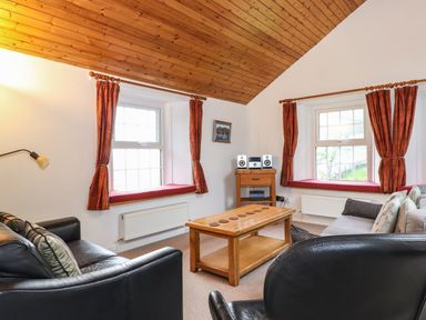 A living room with wooden ceiling brown curtains and black leather sofas at Coombe Cottage in Borrowdale
