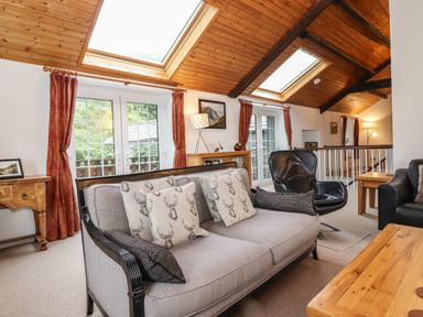 A living room with sofas chairs wooden tables and skylights at Coombe Cottage in Borrowdale