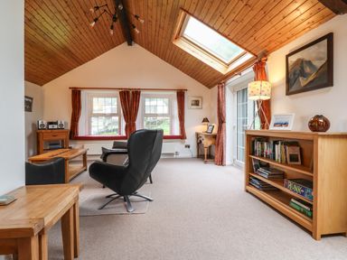 A sitting room with black chairs wooden tables a bookshelf and a skylight window at Coombe Cottage in Borrowdale