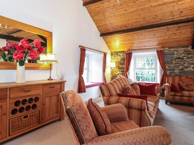 A living room with striped sofas a wooden cabinet with flowers and a large mirror at Coombe Cottage in Borrowdale