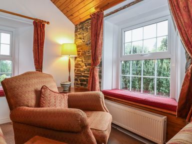 A sitting area with an armchair a side table with a lamp a window with cushions and curtains at Coombe Cottage in Borrowdale