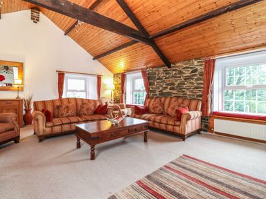 A living room with striped sofas wooden coffee table stone wall and windows at Coombe Cottage in Borrowdale