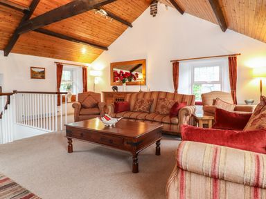 A living room with striped sofas armchairs wooden coffee table and wooden ceiling beams at Coombe Cottage in Borrowdale