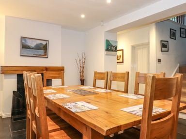A dining room with a wooden table and chairs a painting on the wall and a staircase at Coombe Cottage in Borrowdale