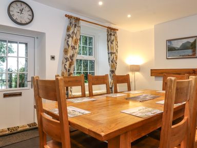 A dining room with a wooden table and chairs near a window and door with curtains at Coombe Cottage in Borrowdale
