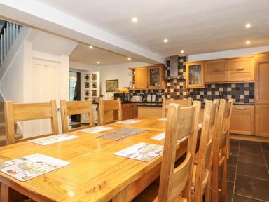 A kitchen with wooden cabinets and a long wooden dining table with chairs at Coombe Cottage in Borrowdale