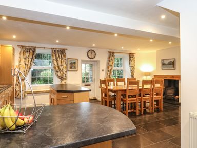 A kitchen and dining area with wooden furniture fruit basket on counter and a stove at Coombe Cottage in Borrowdale