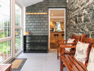 A sunroom with wooden benches and cushions and stone walls at Coombe Cottage in Borrowdale