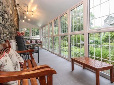 A sunroom with wooden and cushioned seating a wooden bench and stone wall at Coombe Cottage in Borrowdale