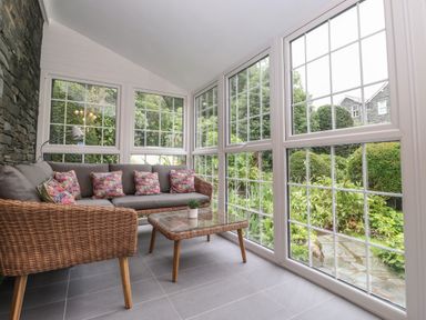 A sunroom with wicker furniture a glass coffee table and large windows overlooking a garden at Coombe Cottage in Borrowdale