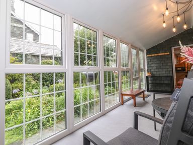 A sunroom with large windows overlooking a garden and chairs with a small wooden table at Coombe Cottage in Borrowdale
