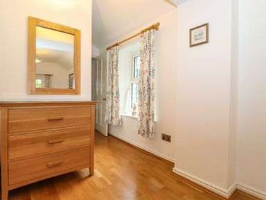 A wooden chest of drawers with a mirror above and a window with floral curtains in a room at Coombe Cottage in Borrowdale