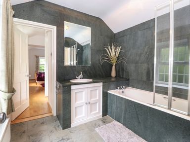 A bathroom with a bathtub a sink with a mirror and a door leading to a bedroom at Coombe Cottage in Borrowdale