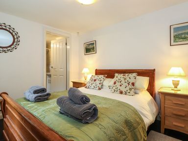 A bedroom with a wooden bed a green bedspread floral pillows bedside tables with lamps and towels on the bed at Coombe Cottage in Borrowdale