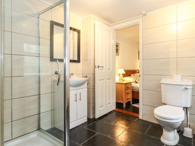 A bathroom with a shower stall sink mirror toilet and an open door leading to a bedroom at Coombe Cottage in Borrowdale