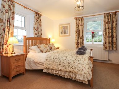 A bedroom with a wooden bed with floral bedding two bedside tables with lamps and floral curtains at Coombe Cottage in Borrowdale