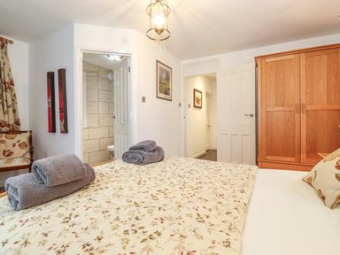 A bedroom with a bed covered with floral bedding towels on the bed a wooden wardrobe and a chair at Coombe Cottage in Borrowdale