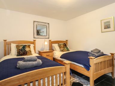 A bedroom with two single beds with wooden frames bedside table lamp and wall mirror at Coombe Cottage in Borrowdale