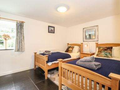 A bedroom with two single wooden beds with blue blankets and towels a window with curtains a nightstand with a lamp and a mirror on the wall at Coombe Cottage in Borrowdale