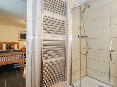 A bathroom with a shower enclosure and towel radiator next to a bedroom with a wooden bed at Coombe Cottage Borrowdale