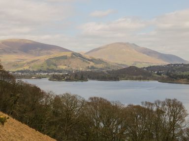 A lake surrounded by trees with hills and a town in the background at St Johns View in Keswick