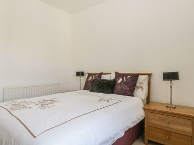A bedroom with a bed with white and purple bedding two bedside tables and lamps at Helvellyn in Keswick