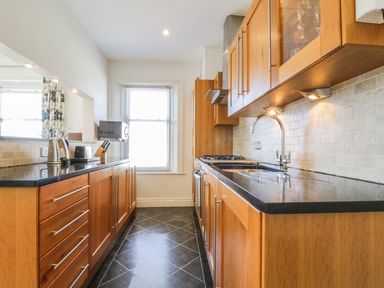 A kitchen with wooden cabinets black countertops a sink a stove a microwave and kitchen appliances at Helvellyn in Keswick