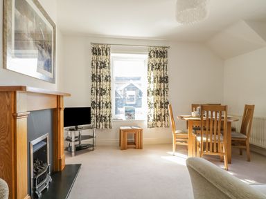 A living room with a fireplace television dining table with chairs and patterned curtains at Helvellyn in Keswick