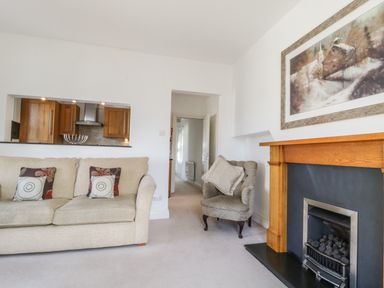 A living room with a beige sofa with cushions a grey armchair a wooden fireplace and a painting above the fireplace at Helvellyn in Keswick