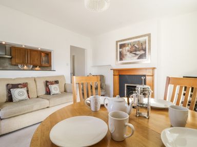 A living room with a wooden dining table set with white cups plates a teapot and a French press next to a beige sofa and a wooden fireplace at Helvellyn in Keswick