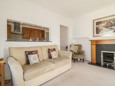 A living room with a beige sofa and armchair a fireplace and a view into the kitchen at Helvellyn Keswick