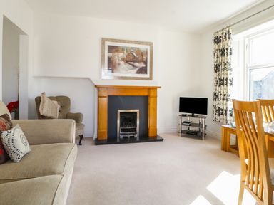 A living room with a fireplace armchairs a television and wooden dining chairs at Helvellyn in Keswick