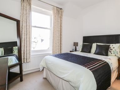 A bedroom with a bed with pillows a bedside table with a lamp a window with curtains and a standing mirror at Helvellyn in Keswick