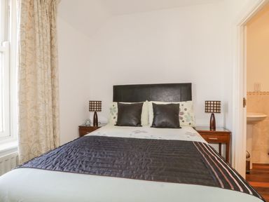 A bedroom with a bed with black and floral pillows bedside tables with lamps and a window with curtains at Helvellyn in Keswick