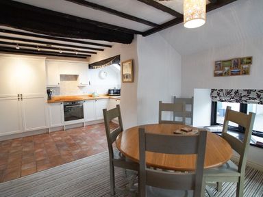 A kitchen and dining area with wooden table and chairs and white cabinets at Laurel Cottage in Spark Bridge