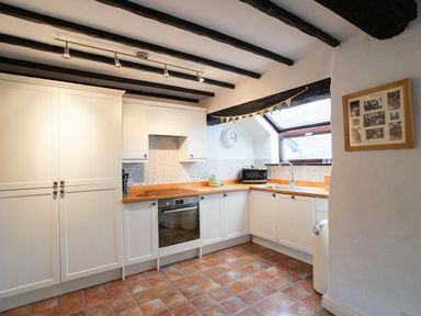 A kitchen with white cabinets wooden countertops a clock and a window at Laurel Cottage in Spark Bridge