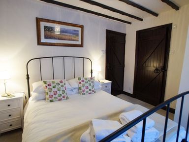 A bedroom with a double bed two patterned pillows two bedside tables with lamps and two dark wooden doors at Laurel Cottage in Spark Bridge