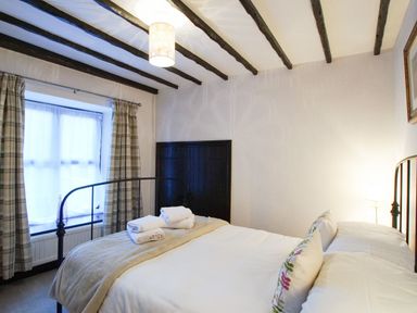 A bedroom with a double bed folded towels on the bed plaid curtains and exposed wooden ceiling beams at Laurel Cottage in Spark Bridge