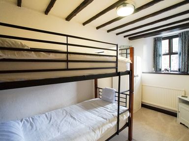 A bedroom with bunk beds a wardrobe a window with curtains and a small cabinet at Laurel Cottage in Spark Bridge