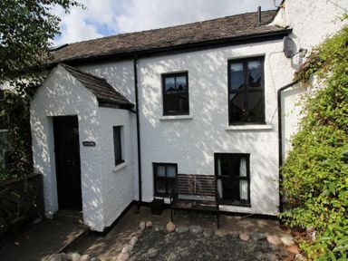 The exterior of a white house with black window frames a brown bench in front and some greenery on the side at Laurel Cottage in Spark Bridge