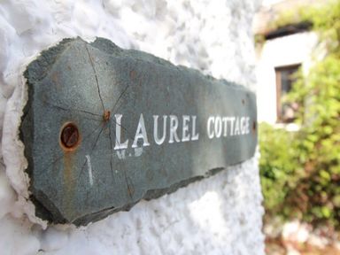 A close up of a stone sign with laurel cottage on a textured white wall with greenery in the background at Laurel Cottage in Spark Bridge