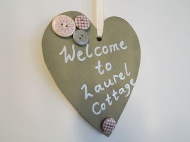 A heart shaped wooden sign decorated with buttons and the text welcome to laurel cottage