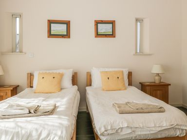 A bedroom with two single beds with wooden frames yellow pillows and folded towels on top at Skiddaw in Cockermouth