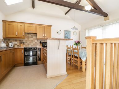 A kitchen with wooden cabinets and a black oven next to a dining area with a table covered by a checkered cloth and wooden chairs at Skiddaw in Cockermouth